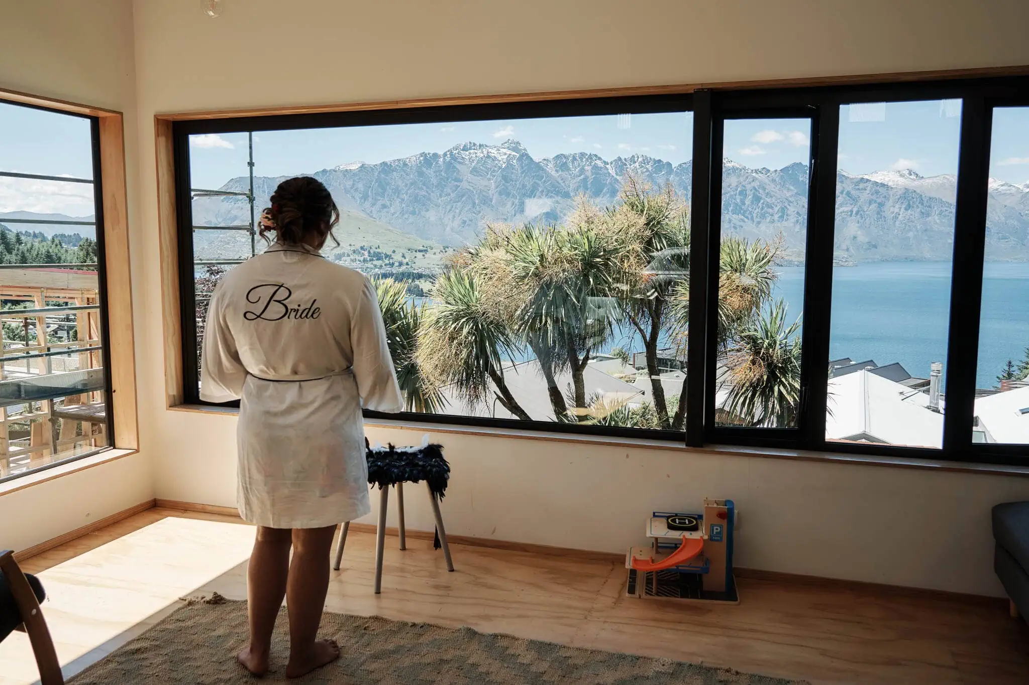 Queenstown New Zealand Elopement Wedding Photographer - A woman, Nikita, in a bathrobe looking out of a window at Coromandel Peak.