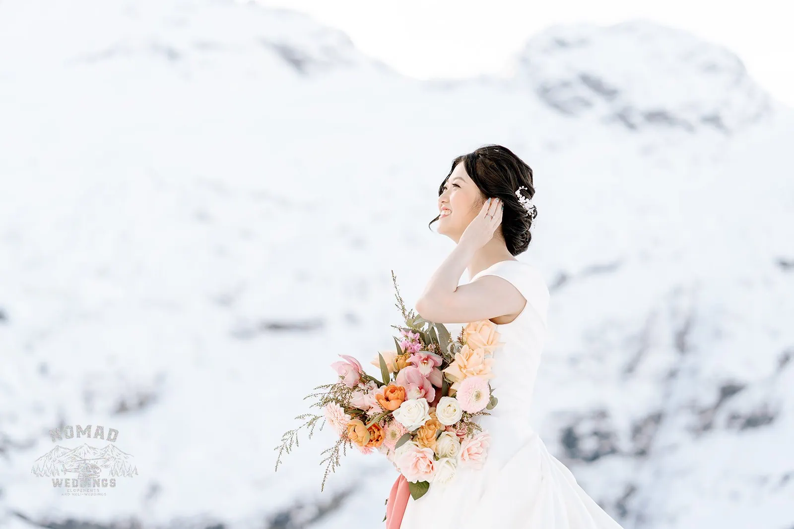 Queenstown New Zealand Elopement Wedding Photographer - A bride in a white dress standing in front of a snow covered mountain during the Bo and Junyi Heli Pre Wedding Shoot.