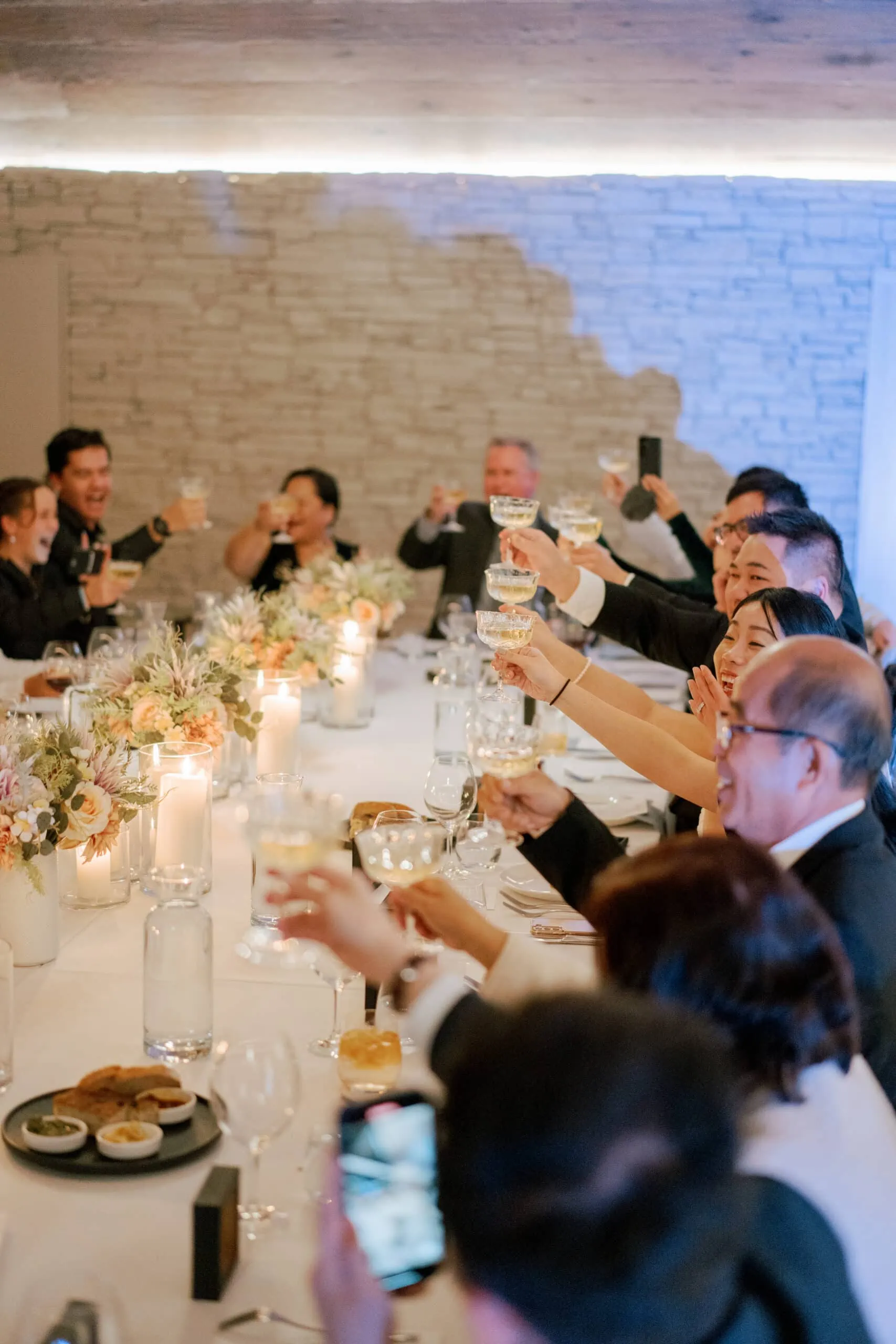 Queenstown New Zealand Elopement Wedding Photographer - A group of people toasting at a Lam and Wendy's Kamana Lakehouse wedding dinner table.