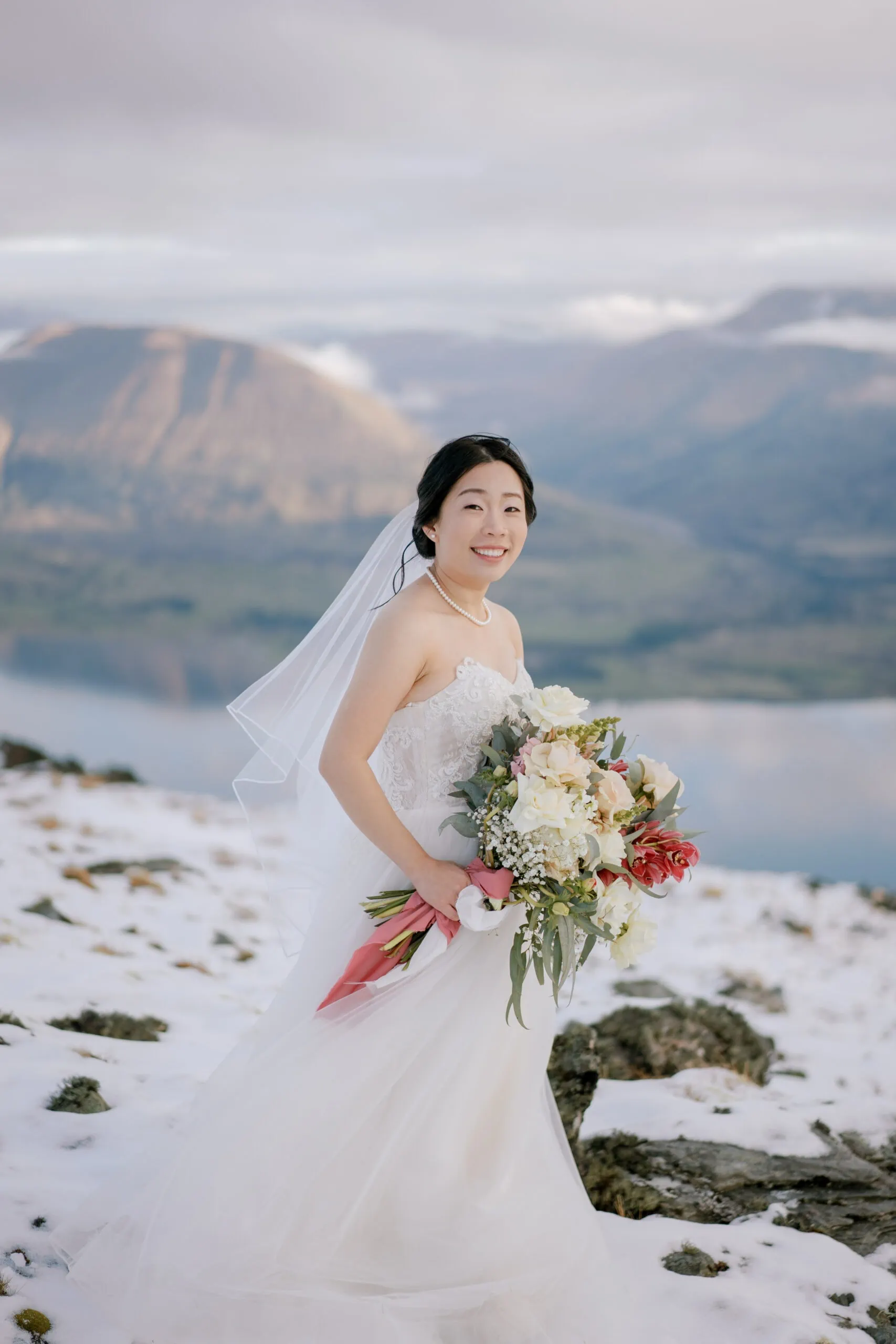 Queenstown New Zealand Elopement Wedding Photographer - A bride in a wedding dress standing on top of a snowy mountain during Lam and Wendy's Kamana Lakehouse Wedding.