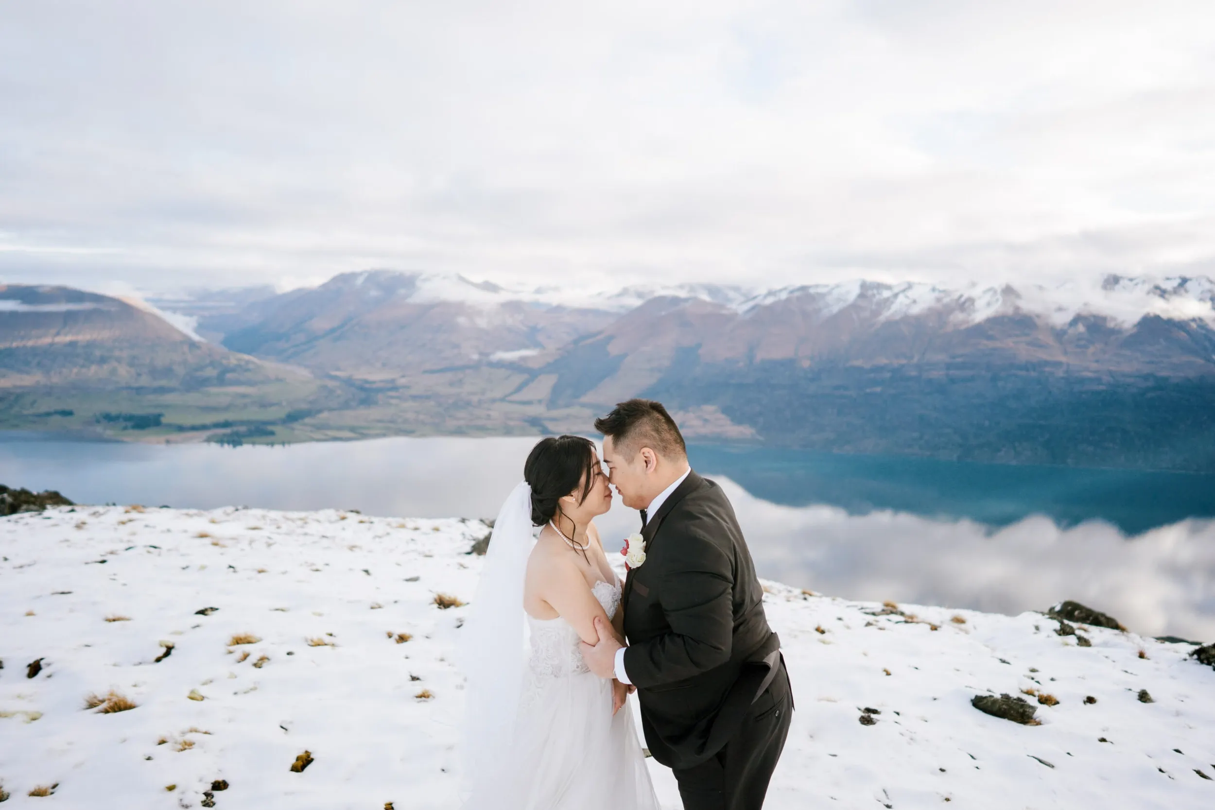 Queenstown New Zealand Elopement Wedding Photographer - Lam and Wendy's Heli Shoot captures a bride and groom kissing on a snow-covered mountain in Queenstown, New Zealand.