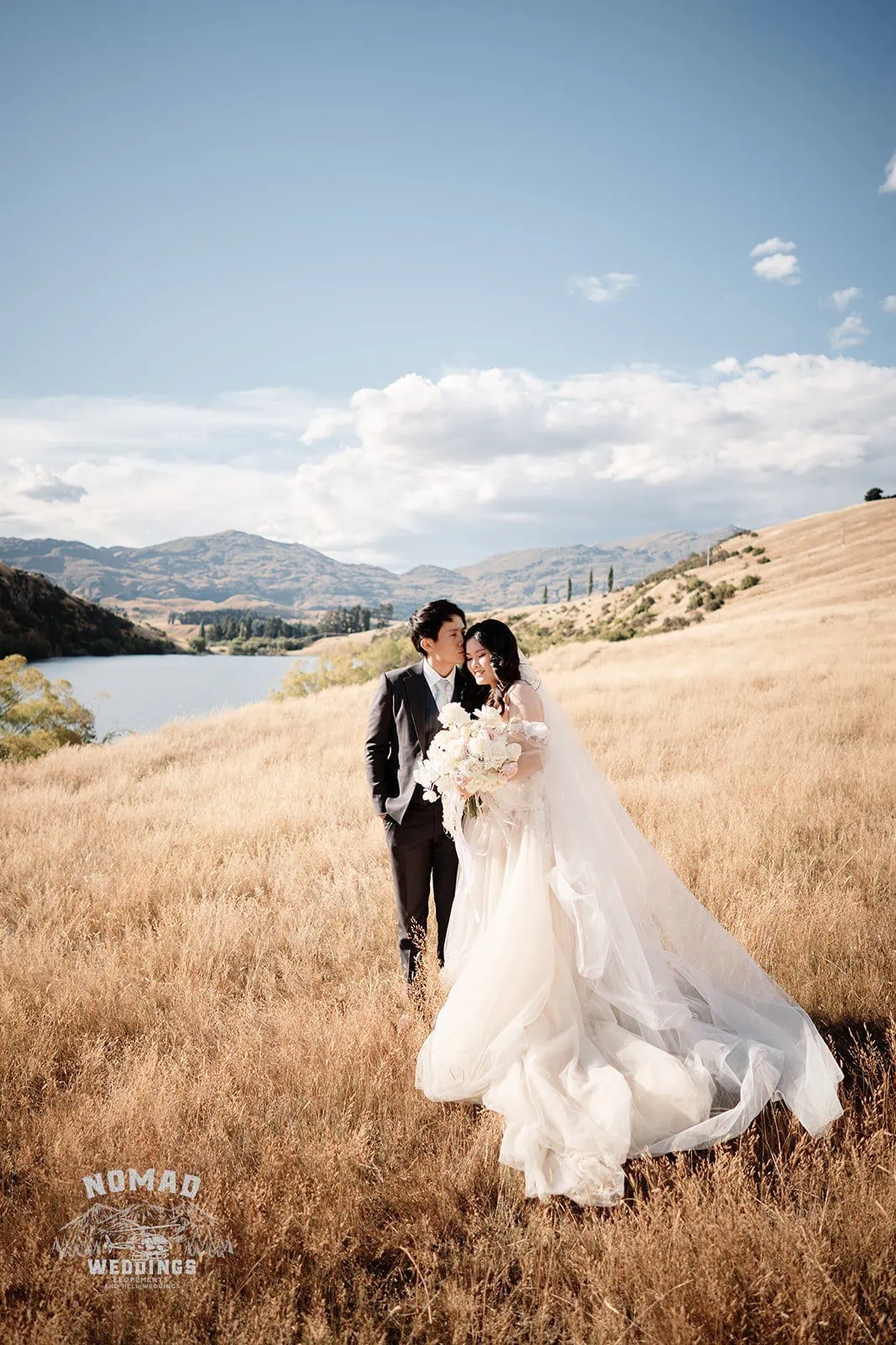 Queenstown New Zealand Elopement Wedding Photographer - A couple embracing in a field with a lake in the background, capturing the essence of summer in Queenstown.