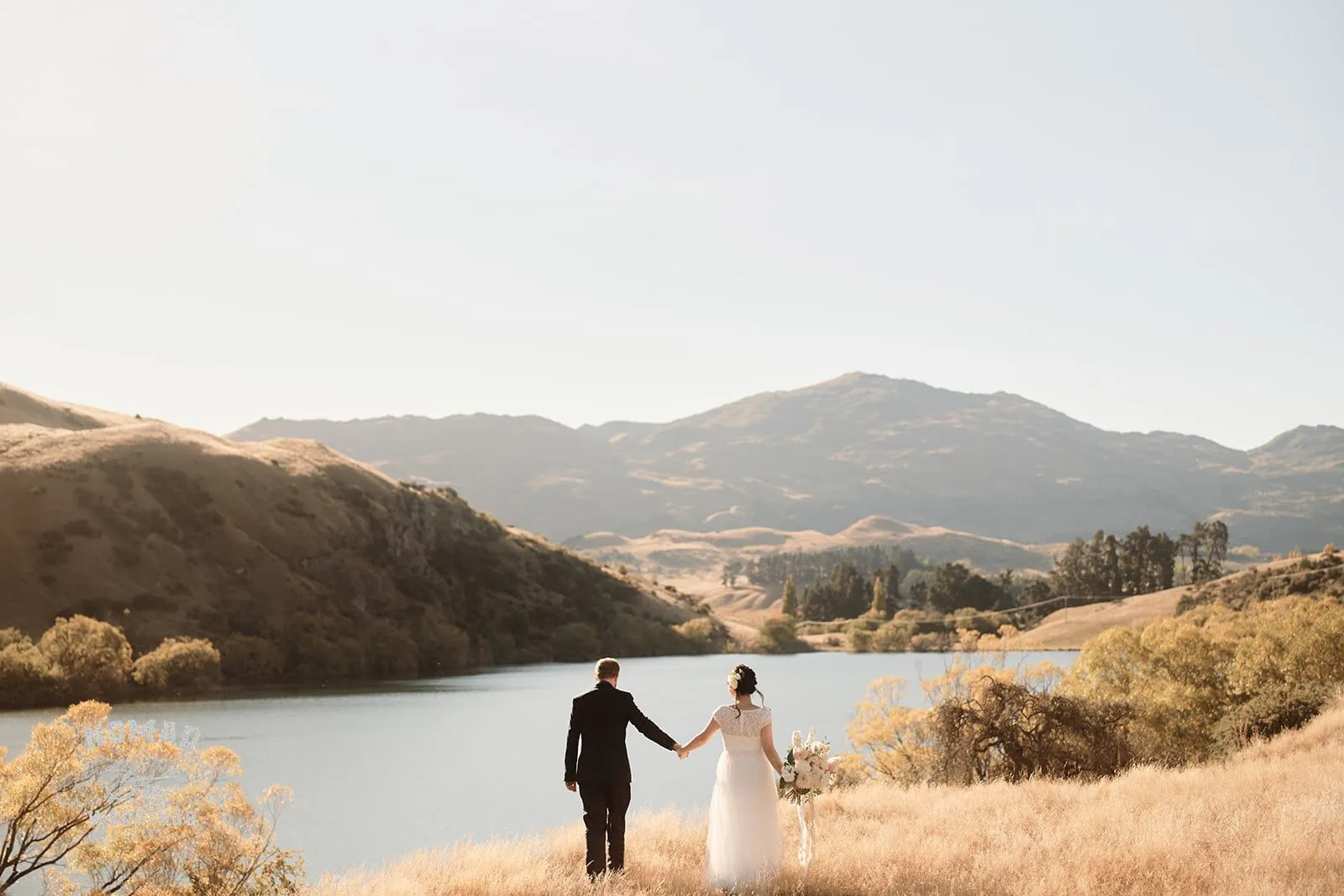 Queenstown New Zealand Elopement Wedding Photographer - A bride and groom standing on a grassy hill overlooking a lake during summer.