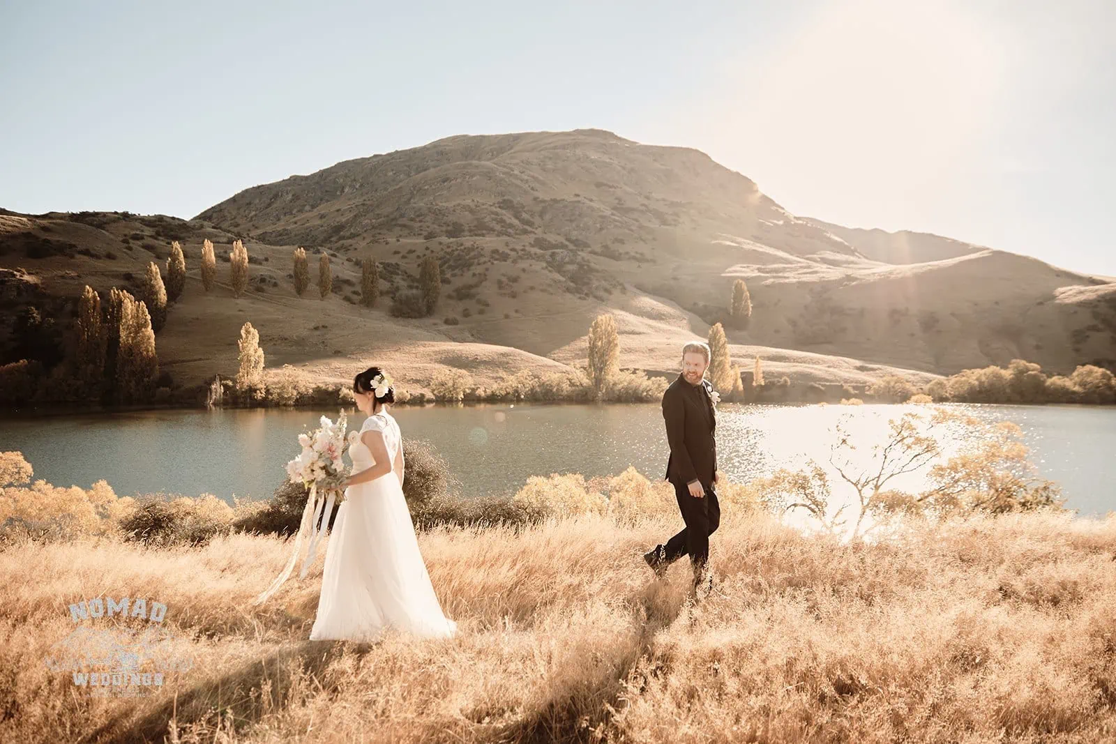 Queenstown New Zealand Elopement Wedding Photographer - A couple posing in a grassy field near a lake for the summer edition of Guide to the Seasons in Queenstown.