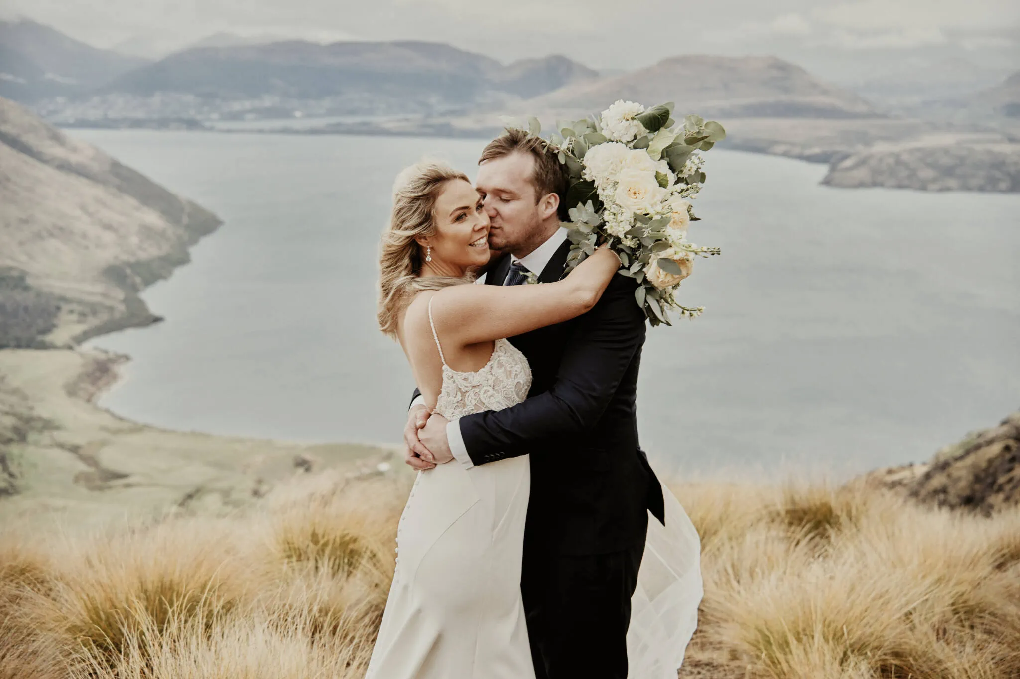 Queenstown New Zealand Elopement Wedding Photographer - Rebecca and Dylan embrace on top of a mountain, overlooking enchanting Moke Lake during their elopement wedding.