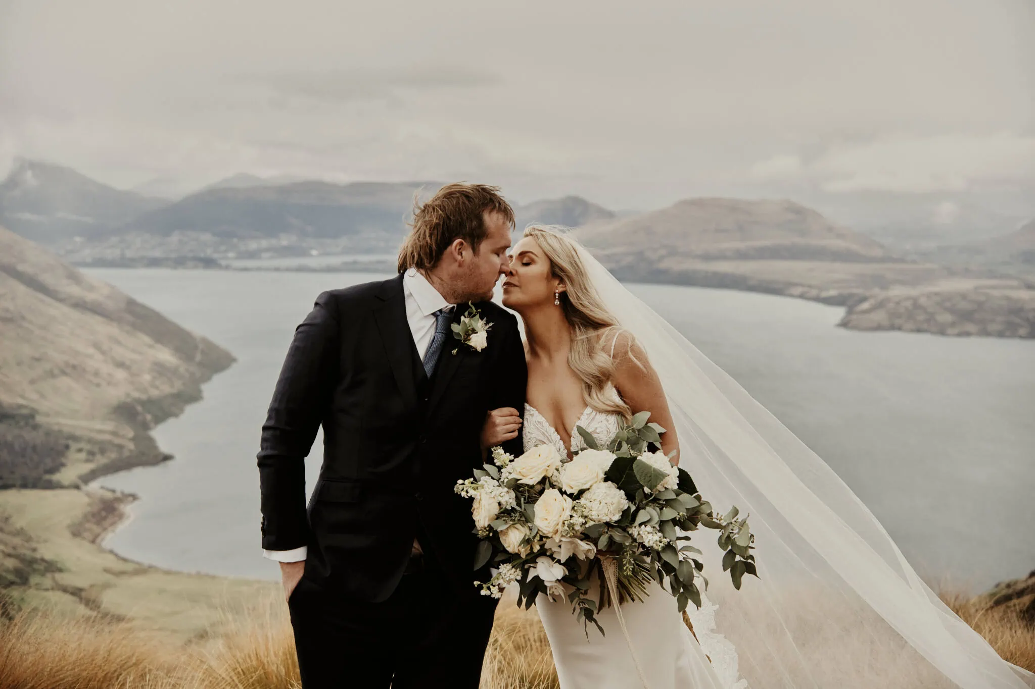 Queenstown New Zealand Elopement Wedding Photographer - Rebecca and Dylan sharing an enchanting kiss on a mountain overlooking Lake Wanaka.