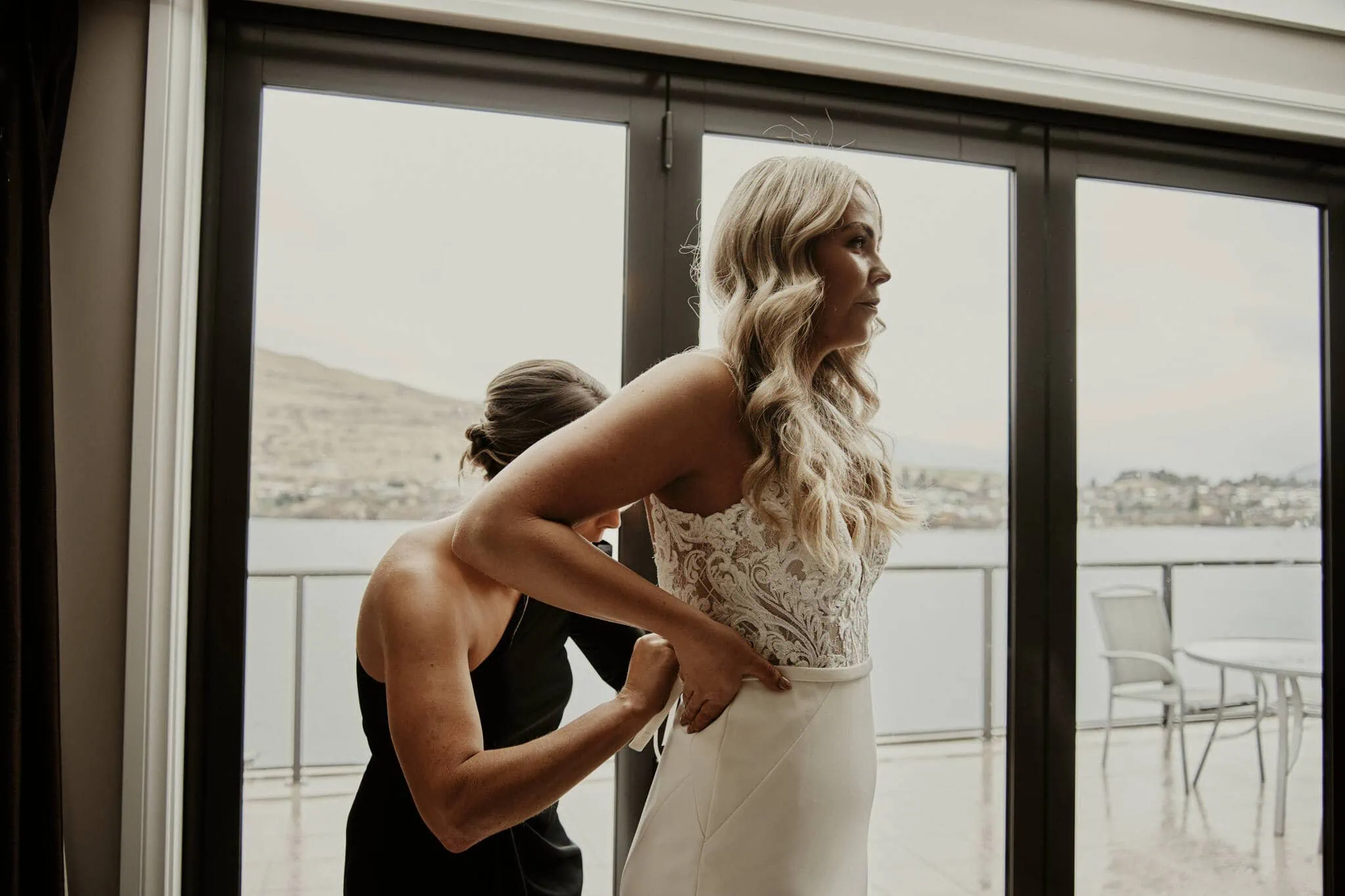 Queenstown New Zealand Elopement Wedding Photographer - A bride, Rebecca, getting ready in a wedding dress in front of a window for her enchanting Moke Lake elopement wedding with Dylan.