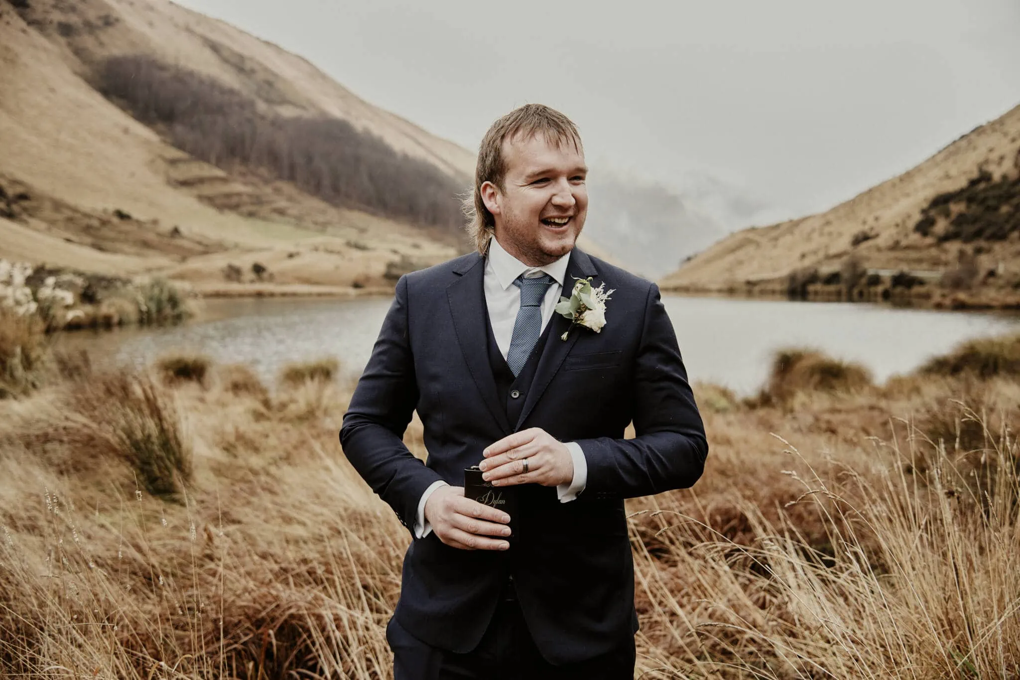 Queenstown New Zealand Elopement Wedding Photographer - A groom in a suit standing in front of a romantic lake during Rebecca and Dylan's enchanting Moke Lake elopement wedding.