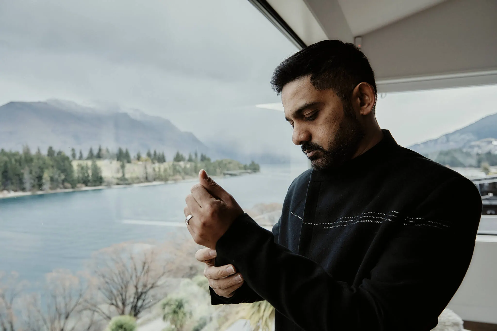 Queenstown New Zealand Elopement Wedding Photographer - A man, Wasim, looking out of a window at Queenstown lake during his Islamic wedding with Yumn.