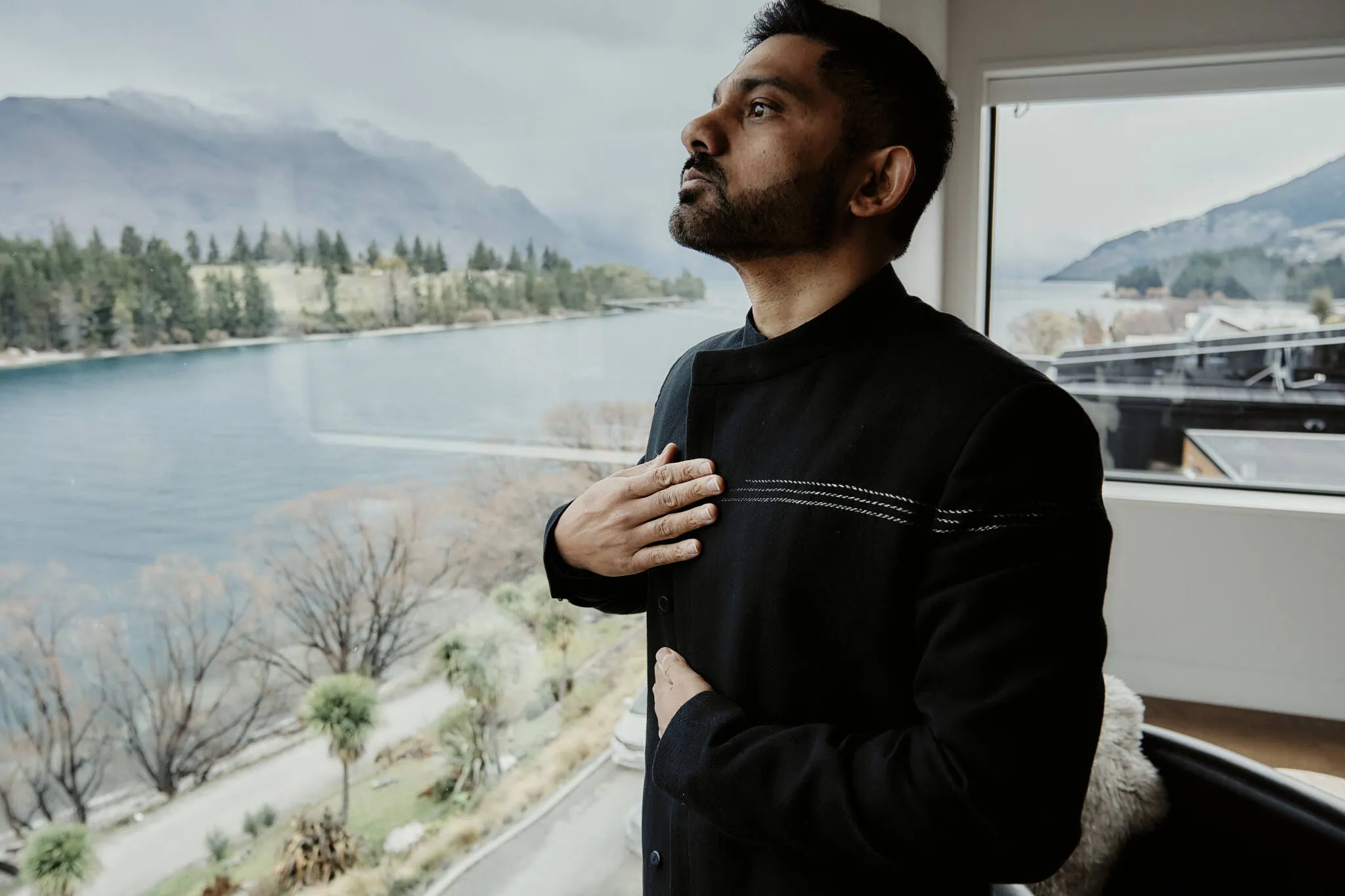 Queenstown New Zealand Elopement Wedding Photographer - A man, Wasim, standing in front of a window with a view of a lake at his Queenstown Islamic wedding.