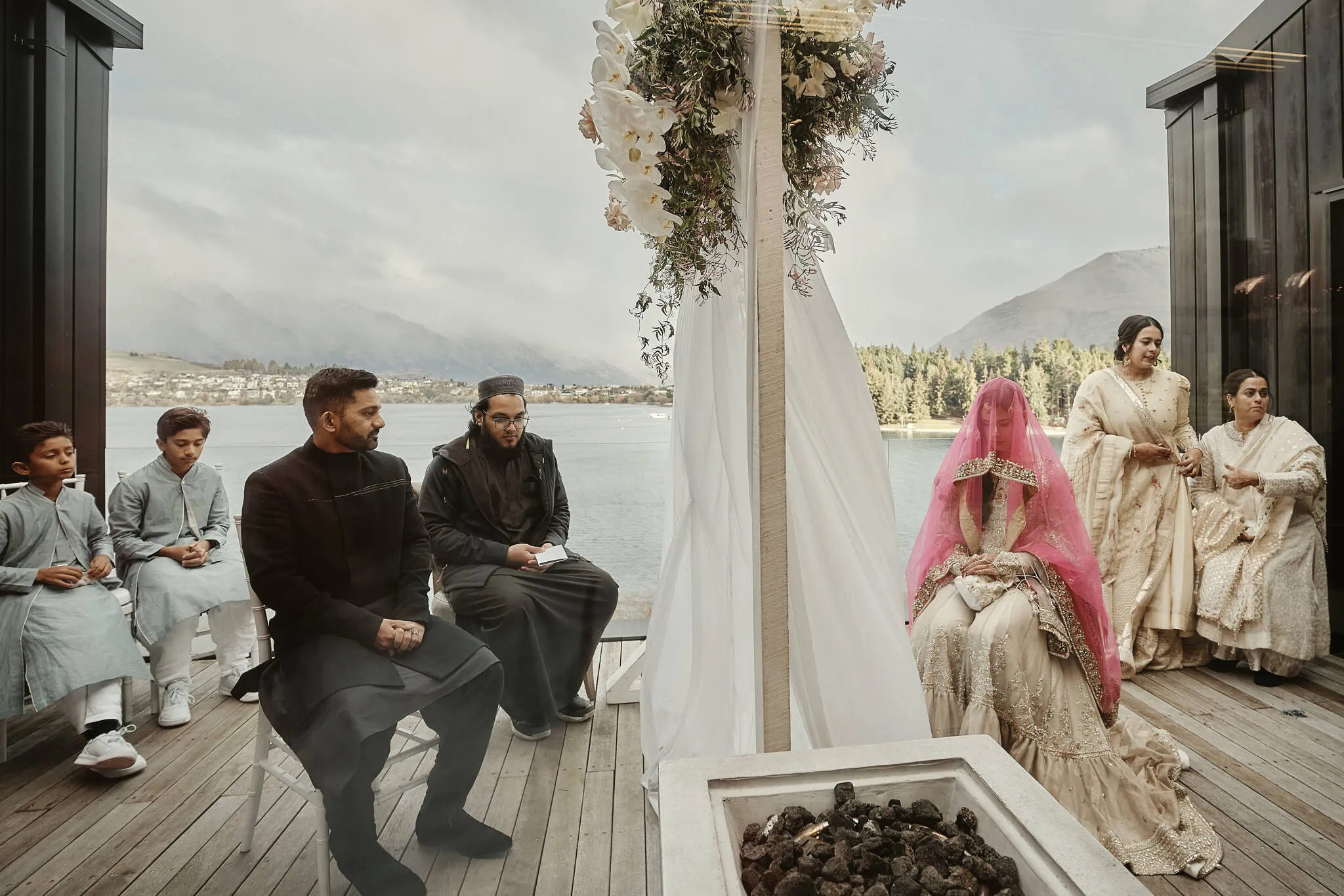 Queenstown New Zealand Elopement Wedding Photographer - Wasim and Yumn's Queenstown Islamic Wedding - A group of people are sitting on a deck in front of a lake.