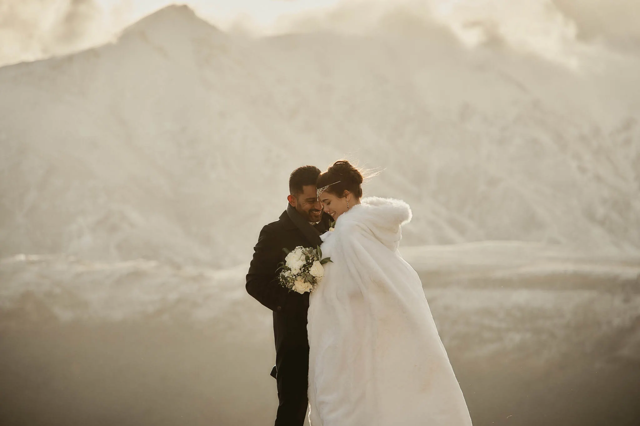 Queenstown New Zealand Elopement Wedding Photographer - Wasim and Yumn, a bride and groom, hugging atop a snowy mountain during their Queenstown Islamic wedding.