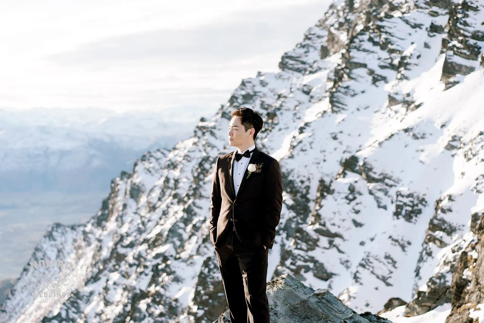 Queenstown New Zealand Elopement Wedding Photographer - A man in a tuxedo stands on top of a snowy mountain during the Bo and Junyi Heli Pre Wedding Shoot.