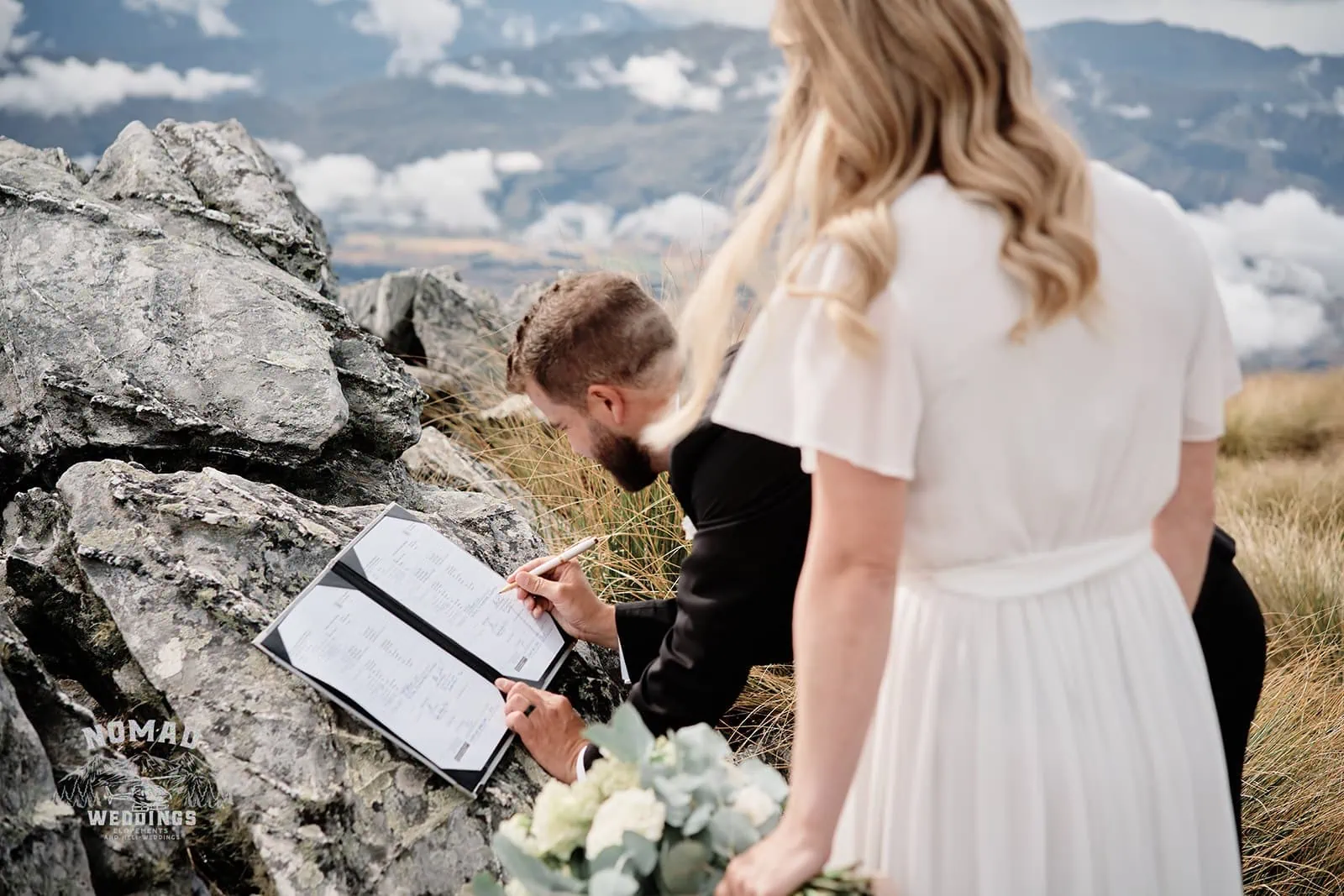 Queenstown New Zealand Elopement Wedding Photographer - A bride and groom signing their wedding vows on top of a mountain in NZ, during the summer.
