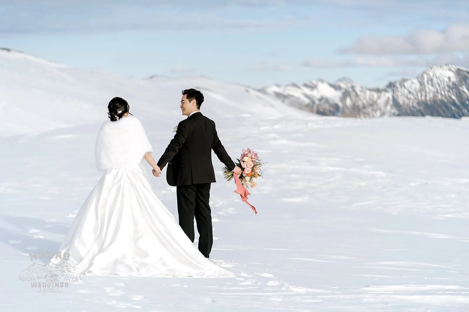 Queenstown New Zealand Elopement Wedding Photographer - Bo and Junyi, a bride and groom, hold hands on a snow-covered mountain during their Heli Pre Wedding Shoot.