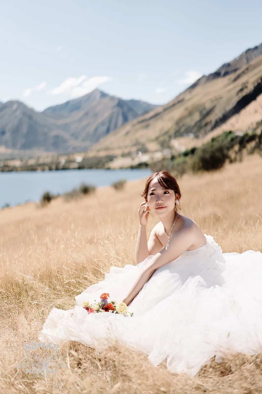 Queenstown New Zealand Elopement Wedding Photographer - A bride sitting in a field with mountains in the background - Queenstown summer edition.