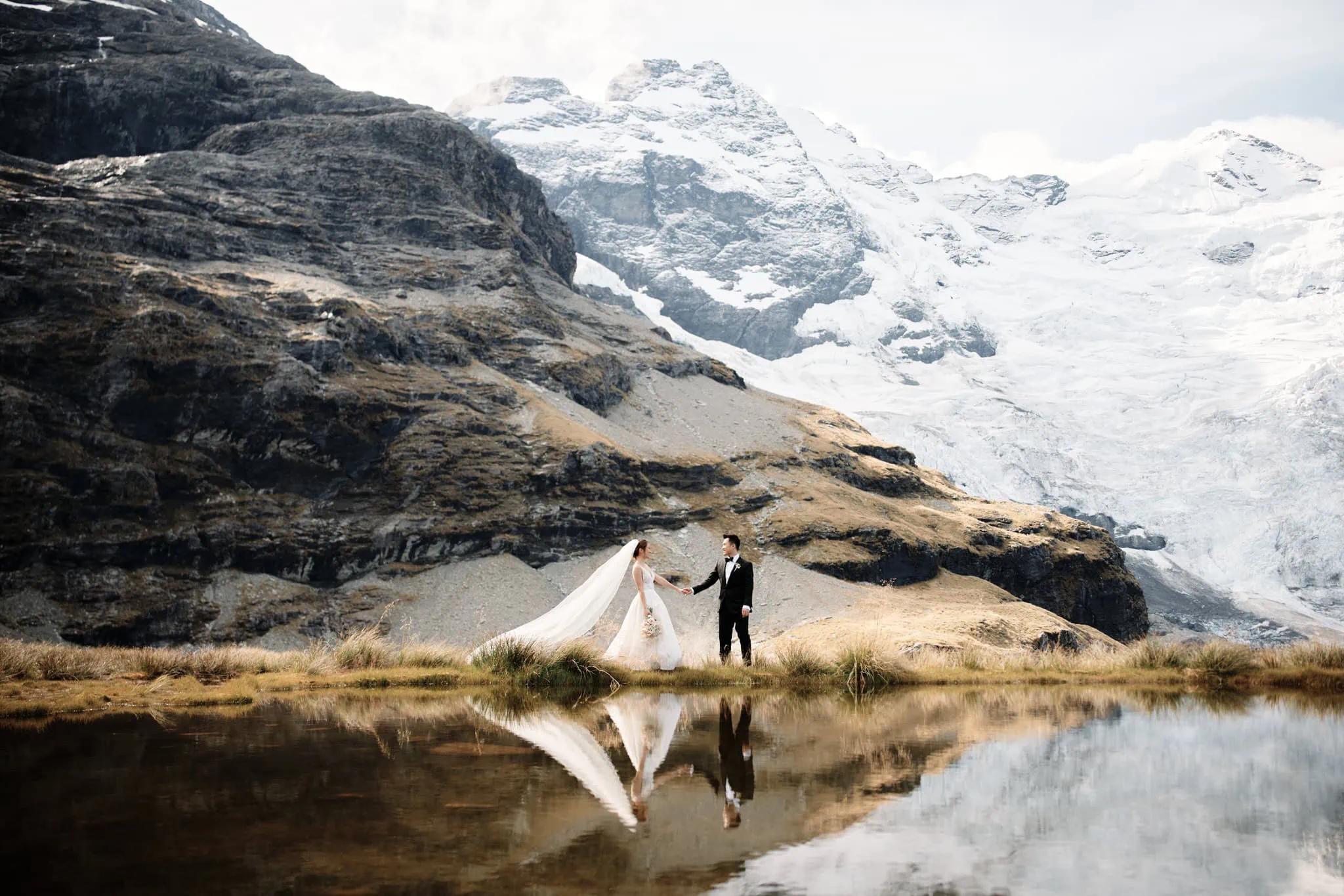 Queenstown New Zealand Elopement Wedding Photographer - A bride and groom posing for wedding photos in front of a scenic lake and mountains.