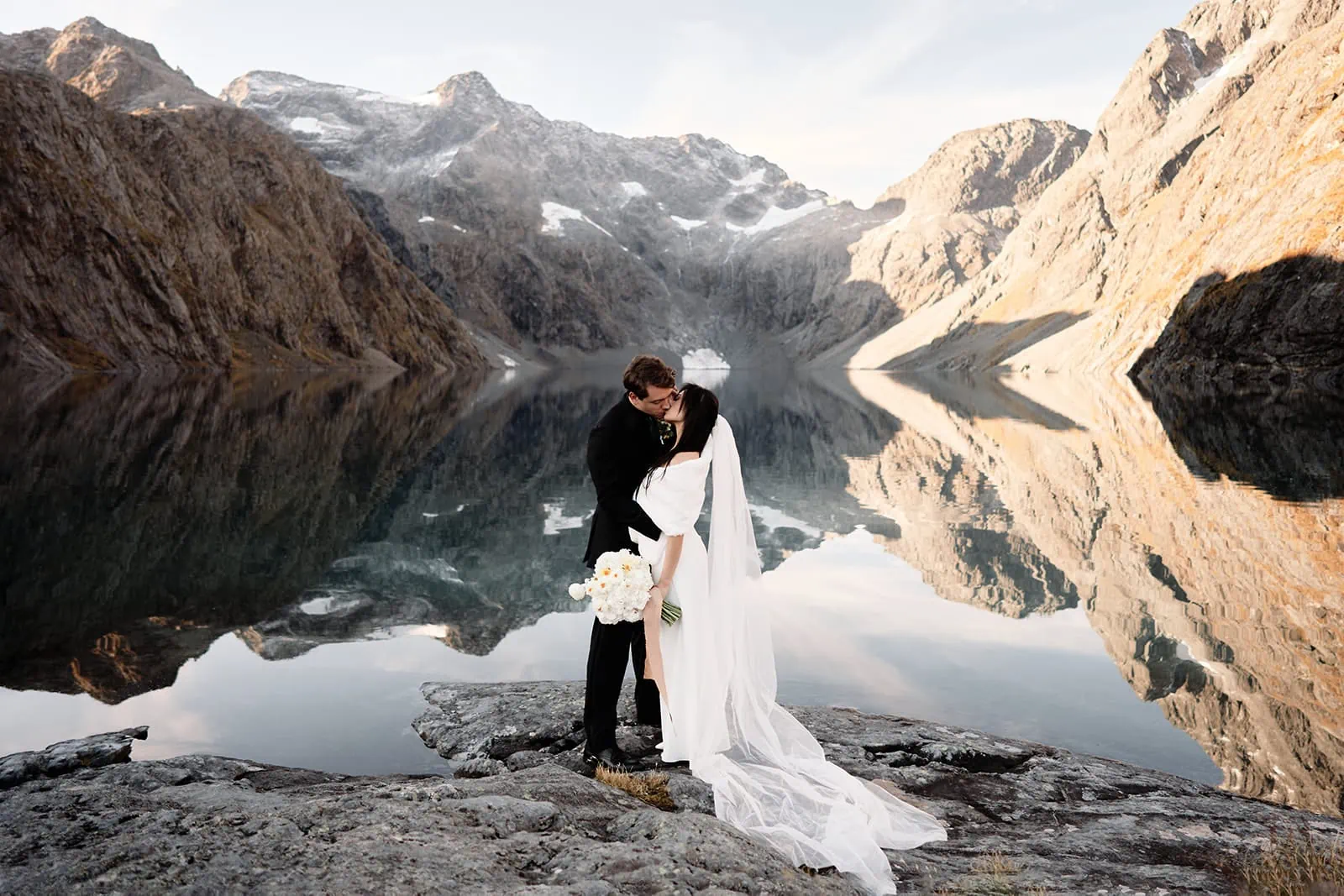 Queenstown New Zealand Elopement Wedding Photographer - A bride and groom embracing their love on their Queenstown Heli-Wedding & Elopement Package, standing in front of a picturesque lake in New Zealand.
