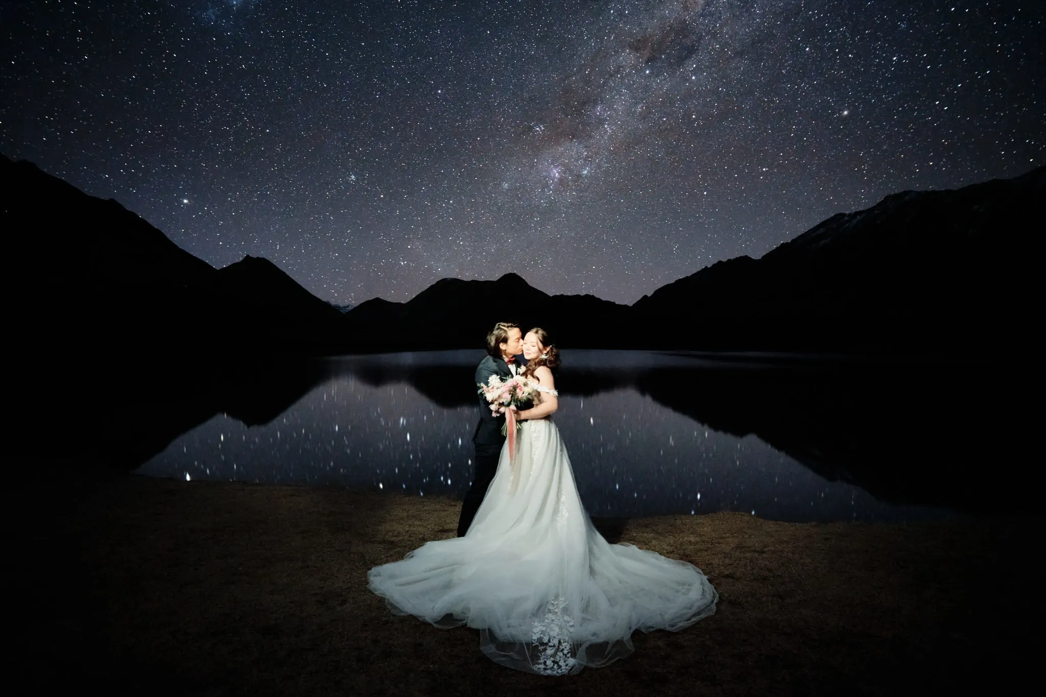 Queenstown New Zealand Elopement Wedding Photographer - A stunning starry night shoot featuring a bride and groom standing under the milky way in front of a lake, beautifully captured for our portfolio.