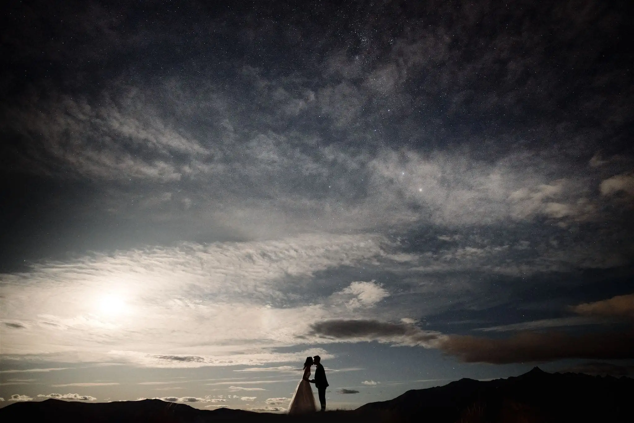 Queenstown New Zealand Elopement Wedding Photographer - A bride and groom standing on top of a mountain under the starry night.