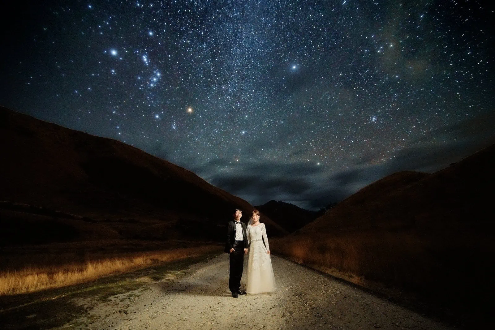 Queenstown New Zealand Elopement Wedding Photographer - A bride and groom standing under the stars on a dirt road during a starry night shoot.
