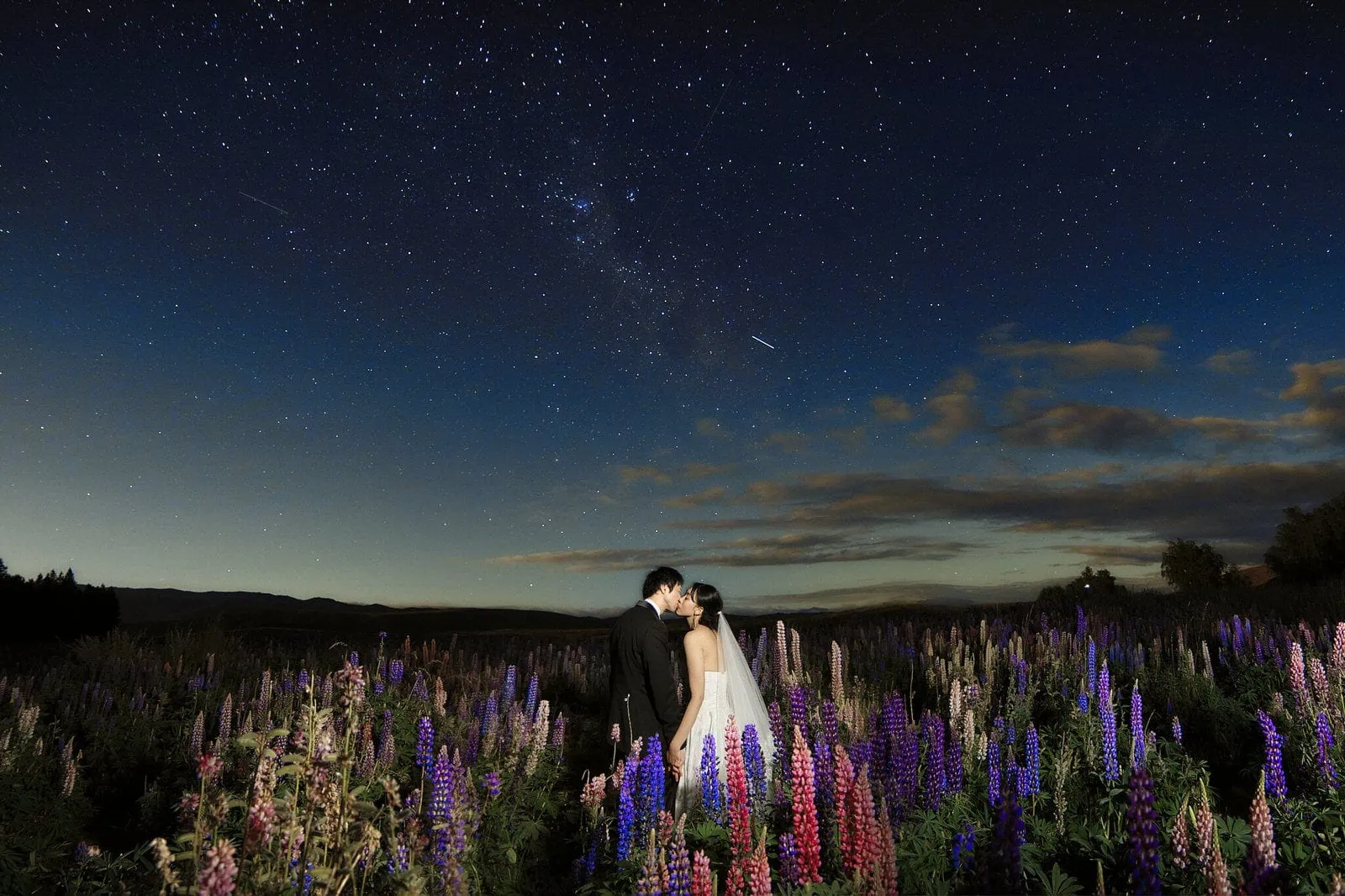 Queenstown New Zealand Elopement Wedding Photographer - A bride and groom embrace passionately under the starry night sky in a field of wildflowers, capturing a dreamy moment for their portfolio shoot.