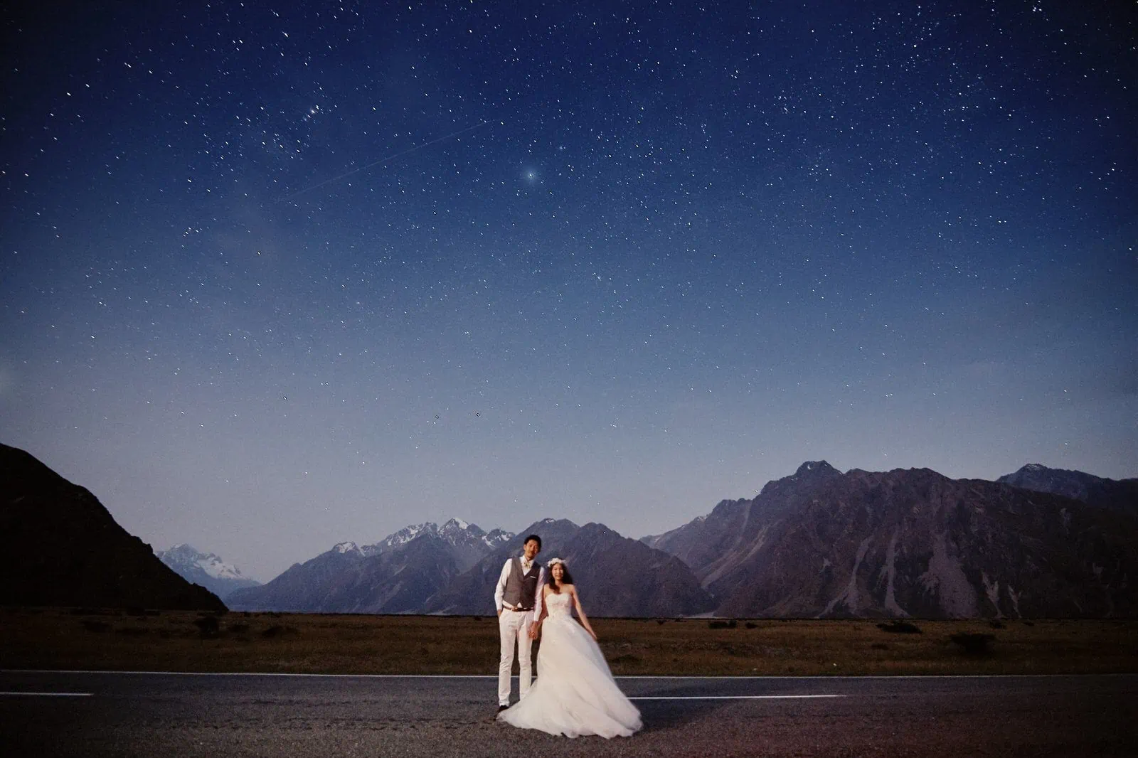 Queenstown New Zealand Elopement Wedding Photographer - A beautiful couple, the bride and groom, bask under the starry night sky on a picturesque road in New Zealand.