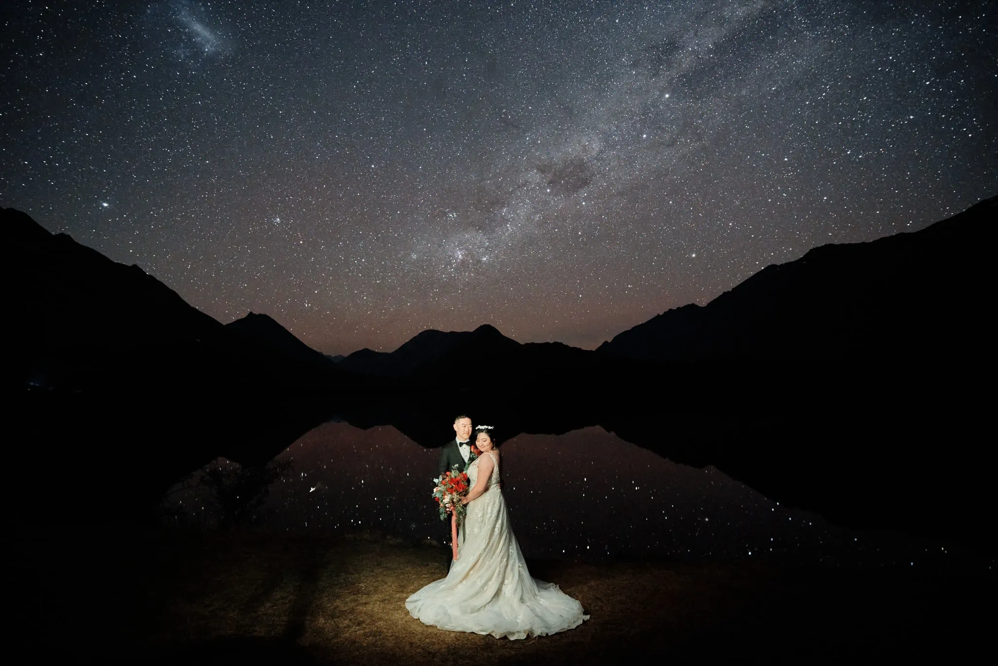 Queenstown New Zealand Elopement Wedding Photographer - A bride and groom standing in front of a lake under the starry night.