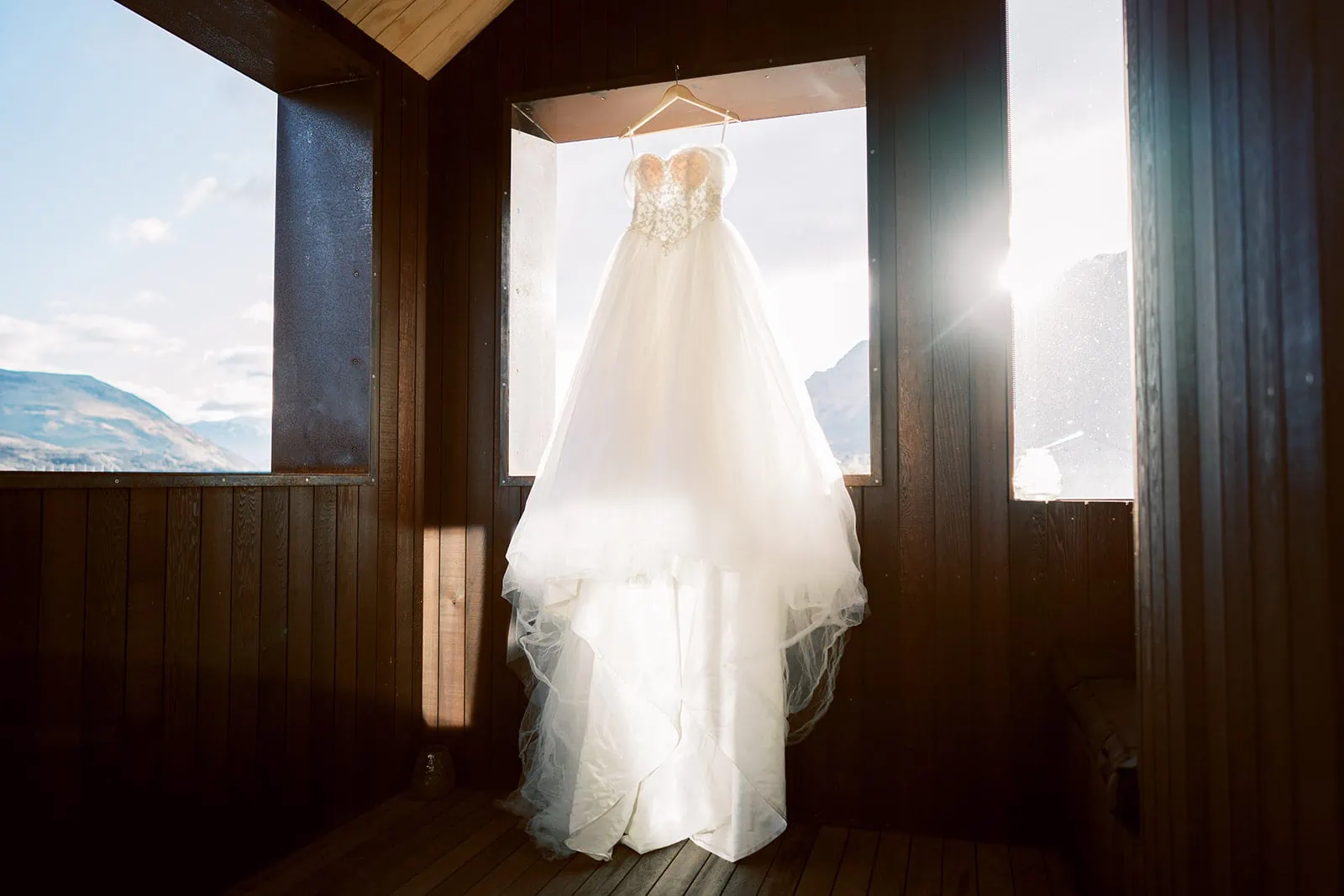 Queenstown New Zealand Elopement Wedding Photographer - A wedding dress hanging from a window in a cabin, emphasizing cost comparison between elopement and traditional weddings.