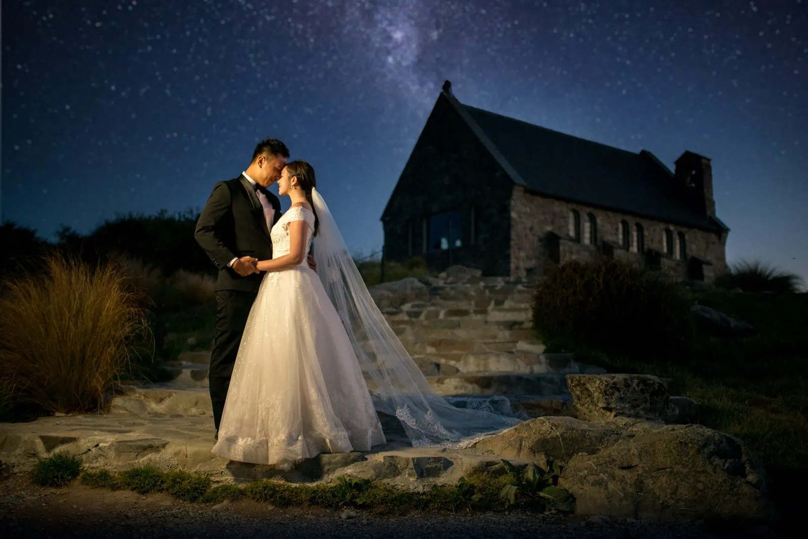 Queenstown New Zealand Elopement Wedding Photographer - A bride and groom have a romantic starry night shoot in front of a church in New Zealand, showcasing their portfolio of stunning wedding photos.