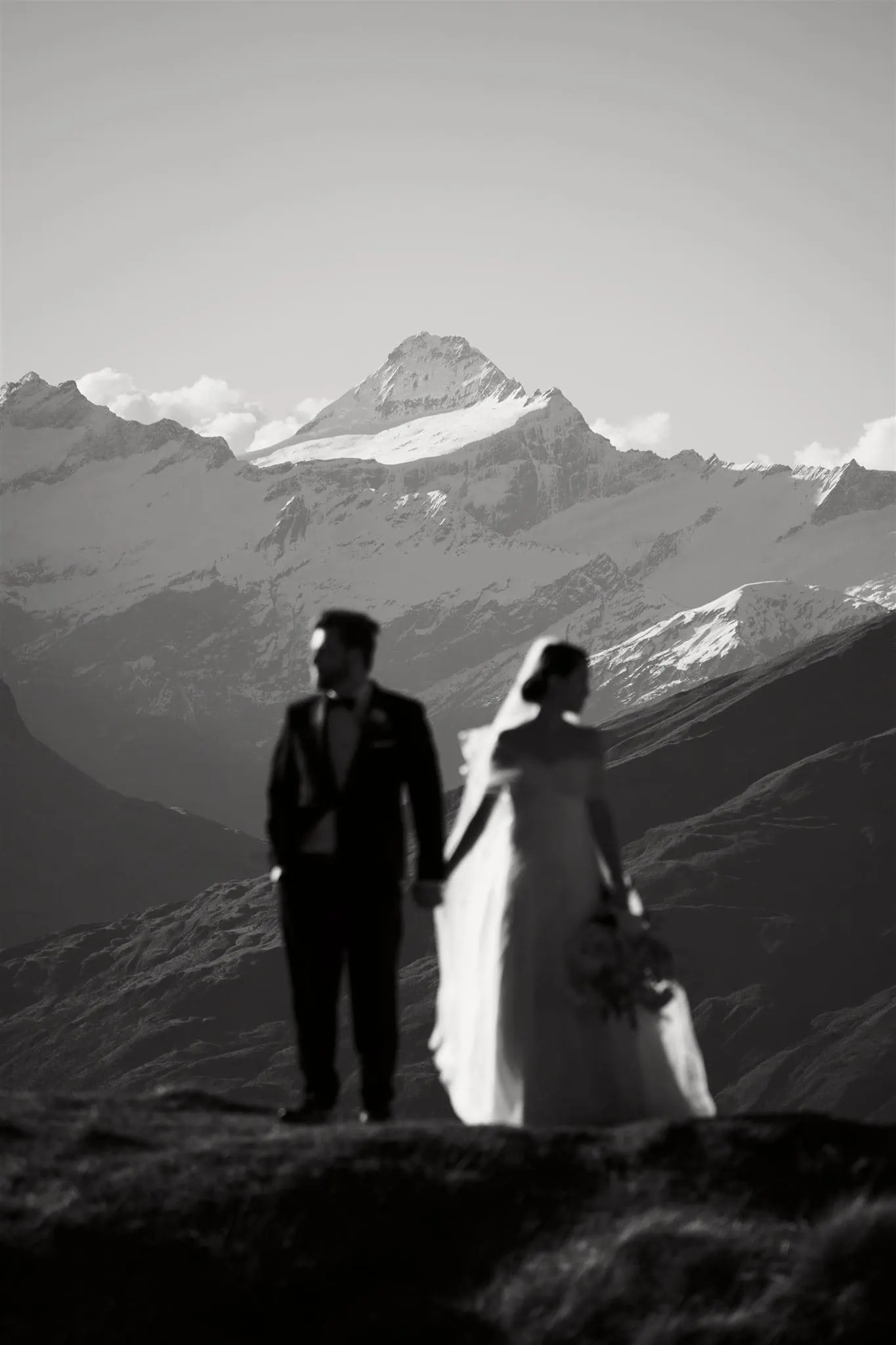 Queenstown New Zealand Elopement Wedding Photographer - A bride and groom enjoying a breathtaking queenstown heli-wedding package, standing on top of a hill with majestic mountains in the background.