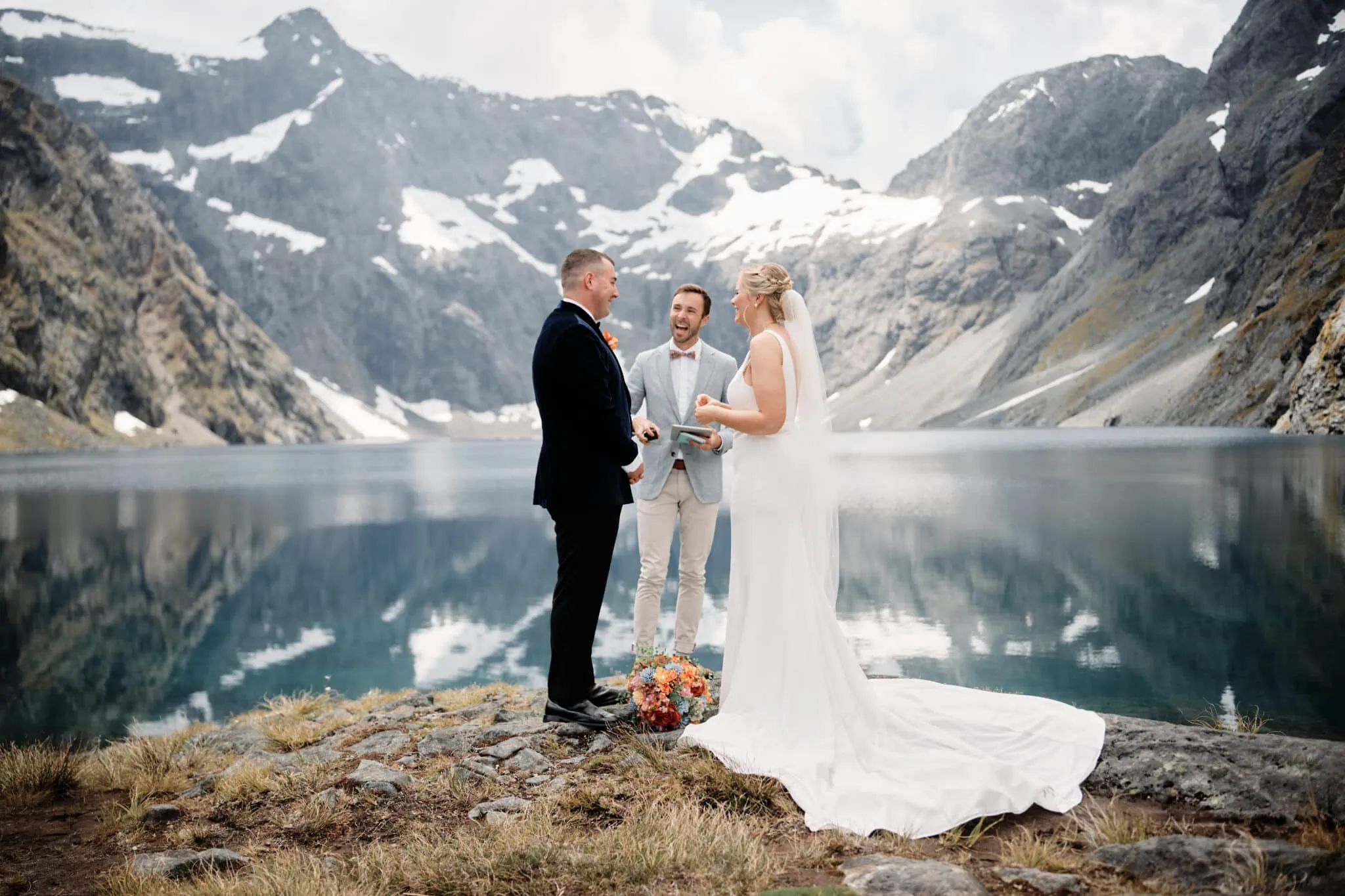 Queenstown New Zealand Elopement Wedding Photographer - An exclusive heli-elopement wedding package featuring a bride and groom standing in front of the majestic Lake Erskine in Fiordland, Queenstown New Zealand.