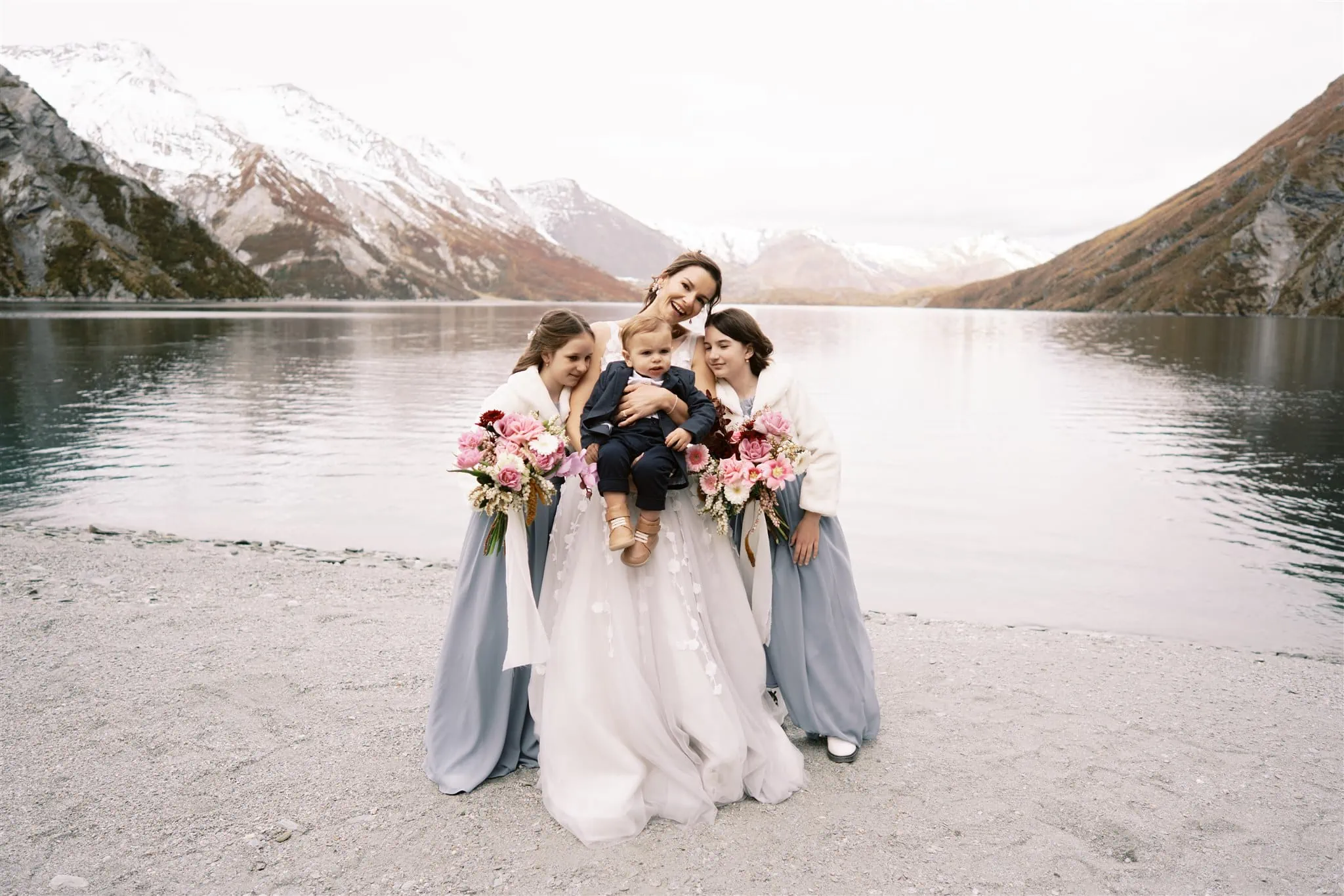 Queenstown New Zealand Elopement Wedding Photographer - Bridesmaids holding a baby in front of a beautiful lake with mountains in the background in Queenstown.