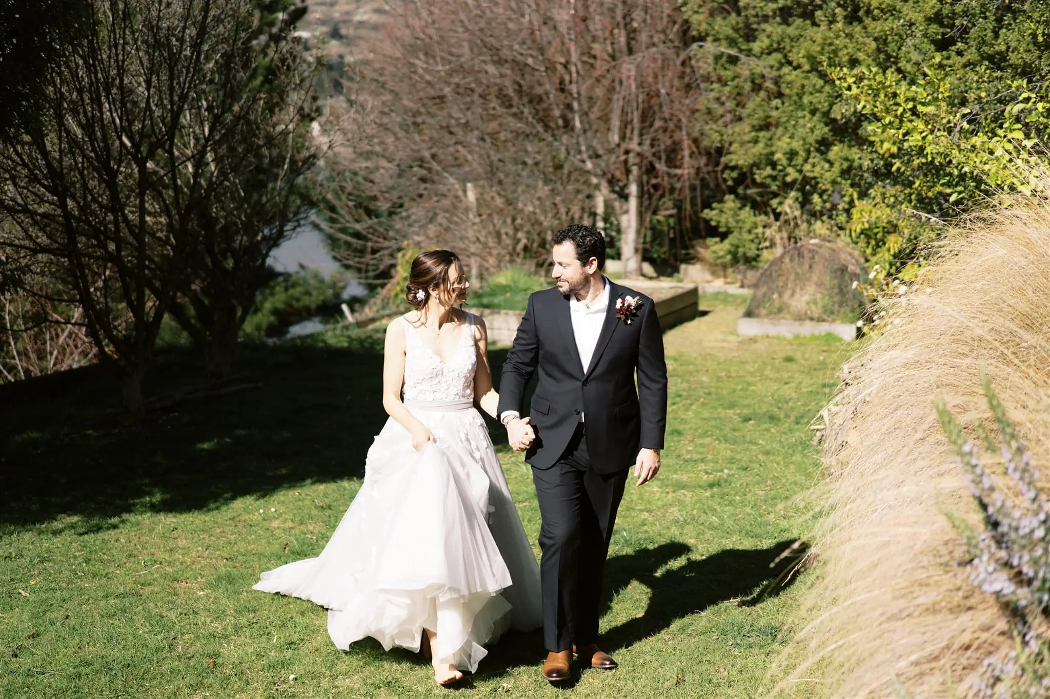 Queenstown New Zealand Elopement Wedding Photographer - A bride and groom, Alex & Shahar, strolling through a scenic grassy field during their Queenstown elopement.