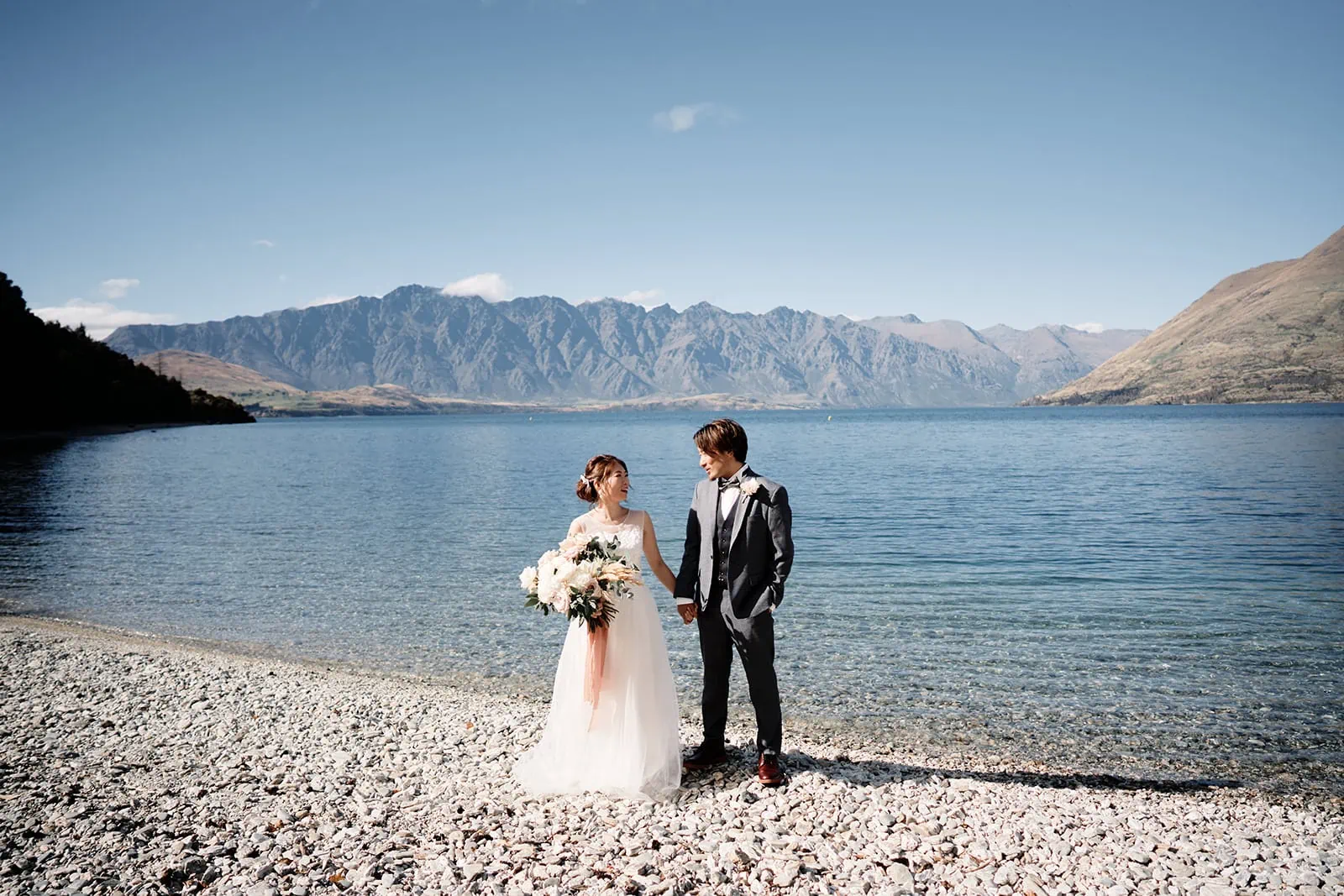 Queenstown New Zealand Elopement Wedding Photographer - A bride and groom standing on the shore of Lake Wanaka, chosen as their Queenstown wedding venue.