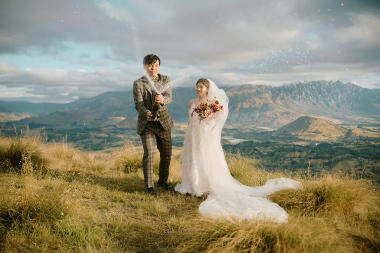Queenstown Elopement Heli Wedding Photographer クイーンズタウン結婚式 | A bride and groom standing on top of a hill in New Zealand for their pre-wedding shoot.
