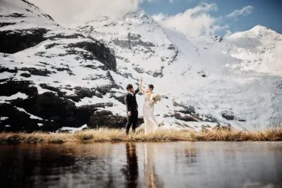 Queenstown New Zealand Elopement Wedding Photographer - A bride and groom standing in front of Earnslaw Burn, with snow capped mountains in the background.