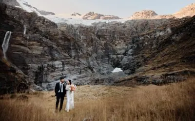 Queenstown New Zealand Elopement Wedding Photographer - A bride and groom standing in front of a breathtaking waterfall in Earnslaw Burn, New Zealand.