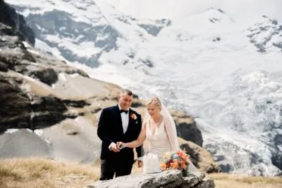 Queenstown New Zealand Elopement Wedding Photographer - Keywords: Earnslaw Burn, snowy mountain.

Description: A bride and groom cutting their wedding cake in front of a snowy mountain at Earnslaw Burn.