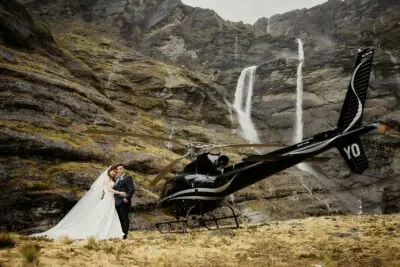 Queenstown New Zealand Elopement Wedding Photographer - A bride and groom standing next to a helicopter in front of a Earnslaw Burn waterfall.