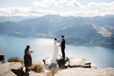 Queenstown New Zealand Elopement Wedding Photographer - A bride and groom standing on the peak of a mountain overlooking lake wanaka.