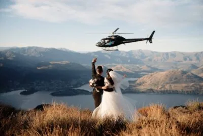Queenstown New Zealand Elopement Wedding Photographer - A bride and groom standing on top of Cecil Peak with a helicopter flying over them.