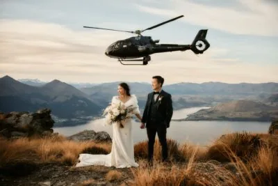 Queenstown New Zealand Elopement Wedding Photographer - A bride and groom embracing atop Cecil Peak, with a helicopter in the background.