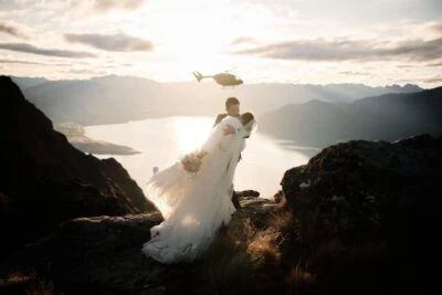 Queenstown New Zealand Elopement Wedding Photographer - A bride and groom standing on top of Cecil Peak, with a helicopter in the background.