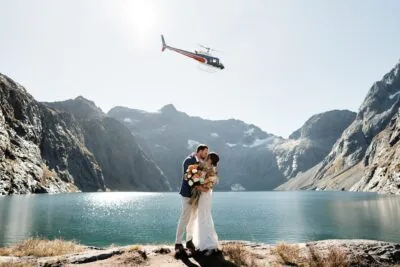 Queenstown New Zealand Elopement Wedding Photographer - A bride and groom standing in front of a Erskine lake with a helicopter in the background.