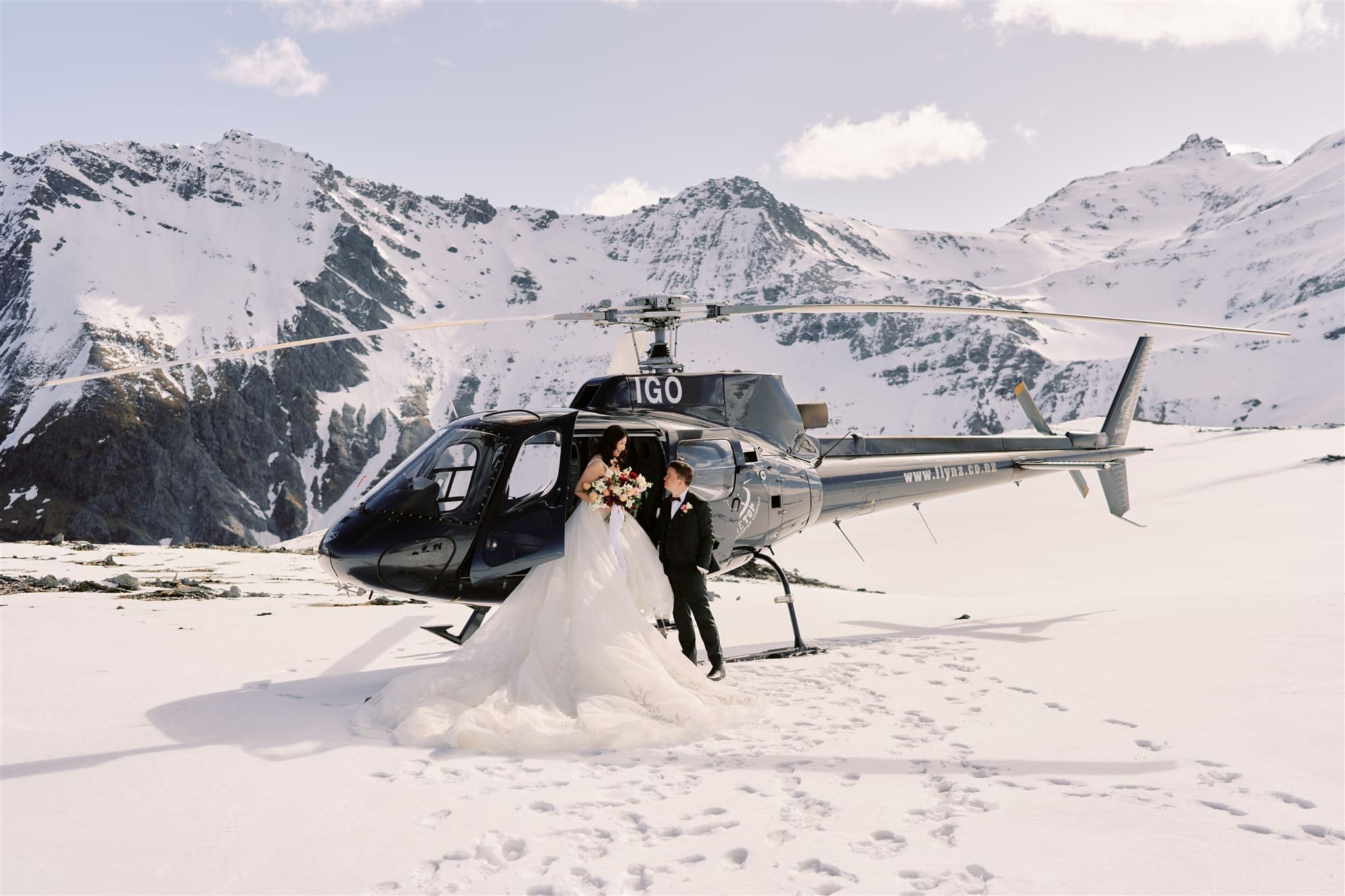 Queenstown New Zealand Elopement Wedding Photographer - A Queenstown Heli-Wedding couple standing next to a helicopter in the snow.