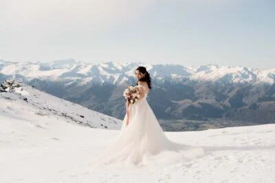 Queenstown New Zealand Elopement Wedding Photographer - A bride standing on top of the Remarkables, a snowy mountain range, with mountains in the background.