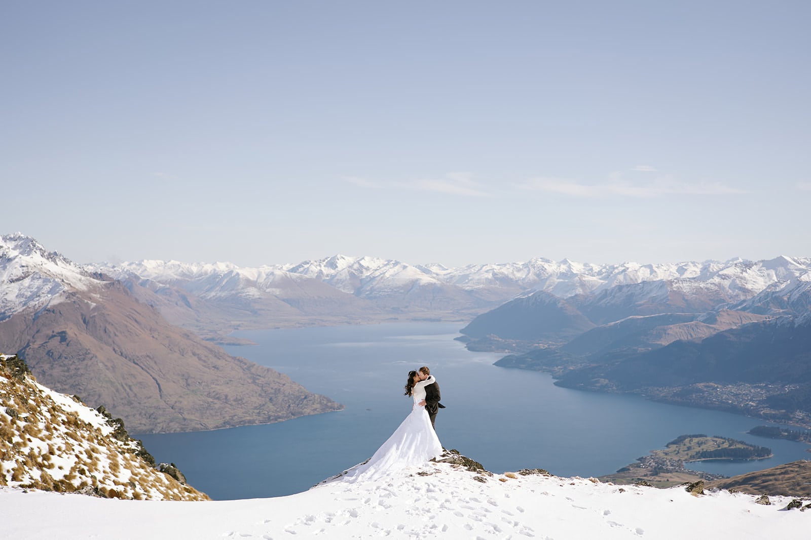 Queenstown New Zealand Elopement Wedding Photographer - A bride and groom, captured by a Queenstown Wedding Videographer on the Remarkables, standing on top of a snowy mountain overlooking lake wanaka.