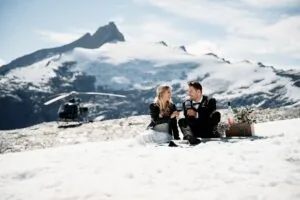 Queenstown New Zealand Elopement Wedding Photographer - A bride and groom sitting on the snow in front of a Tyndall Glacier.