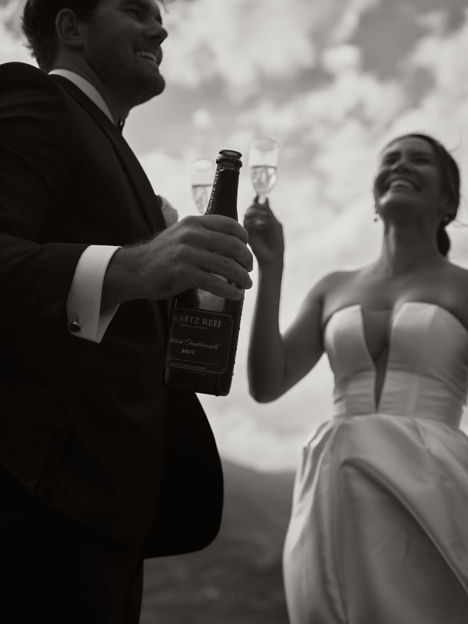 Queenstown Wedding Photographer Contact: A bride and groom toasting with a bottle of wine in this beautiful wedding picture.